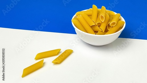 Tableau sur toile A white bowl of dry penne pasta on a blue and white background with plenty of space for text