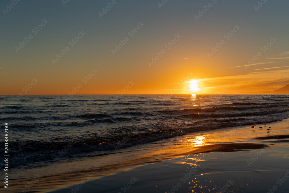 Fototapeta premium Golden sunset over calm sea waves reflecting on the wet sand, creating a peaceful and dreamy seascape with warm light and soft evening atmosphere
