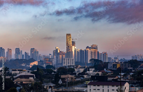 Curitiba, Brazil - June 16 2025: Cityscape with skyscrapers in the background and houses and trees in the foreground under a cloudy sky during twilight.