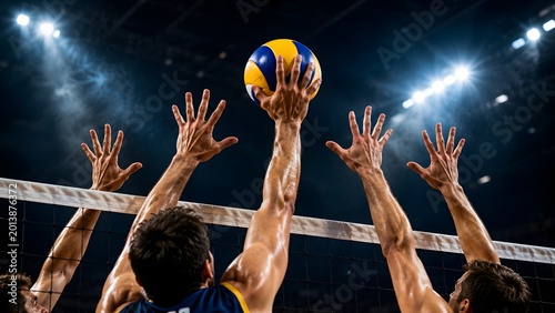 Volleyball players hands jumping at net blocking spike attack ball in indoor stadium, professional sports action during competitive match game with dramatic arena lighting
