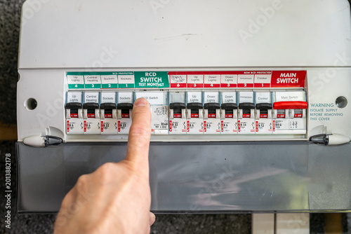 фотографія Person flicking a switch on a UK consumer unit, also known as a fuse box or distribution board, inside a residential property