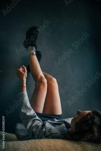 Beautiful young girl with beautiful legs exuding carefree youthfulness while lying relaxed in a cozy atmosphere, highlighting comfort and playful vibes in a dynamic composition.