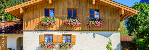 Quadro su tela Wooden house with flower boxes in a sunny landscape near tall trees in summer