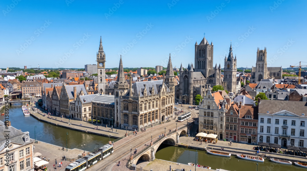 Obraz premium Panoramic aerial view of the historic city center of Ghent, Belgium, with canals and medieval architecture under a clear blue sky.