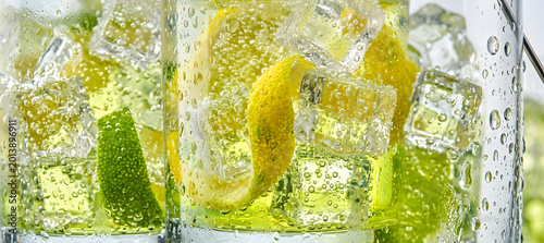Macro close up of refreshing soda with lemon and lime. Fizzy sparkling water with ice cubes and citrus zest background