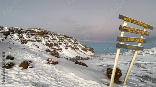 Breathtaking sunrise at Stella Point on the way to Kilimanjaro summit, Tanzania. Snowy mountain landscape with a congratulations sign at 5756 meters altitude. Extreme trekking. 4K