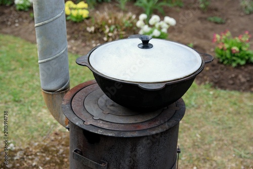 Foto Traditional kazan with lid on a wood-burning stove in a blooming garden backgrou