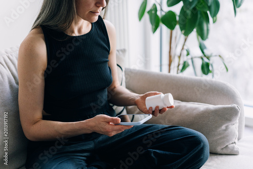 Woman taking a pill while using a phone in a living room