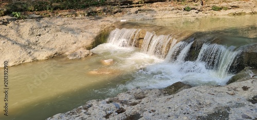 Small natural waterfall flowing through rocky stream in forest landscape