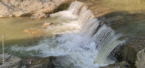 Small natural waterfall flowing through rocky stream in forest landscape