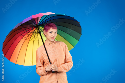 Person holding rainbow umbrella standing on blue background