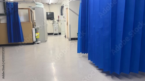 Panning shot of empty cubicles in hospital ward. Blue partitioning curtains hanging open as there are no patients at this time.