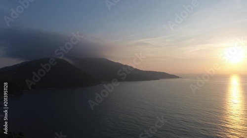 Dramatic sunrise over mountain landscape with soft clouds drifting across peaks. Tropical greenery and jungle blending into coastline with ocean in the background