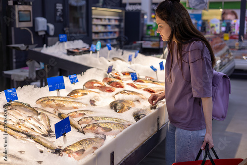 Cuadro en lienzo Woman choosing fresh fish at supermarket seafood counter