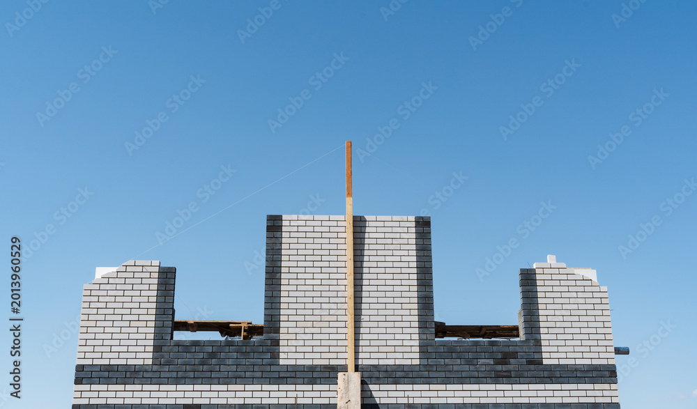 Obraz premium Unfinished Concrete Framework Stands Tall Against Bright Blue Background. Partially Completed Cinderblock Construction With Central Timber Support Visible Against Clear Sky