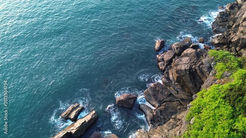 Drone footage of ocean waves hitting rocky shore during sunrise. Calm yet powerful coastal scenery with golden morning light and turquoise water.