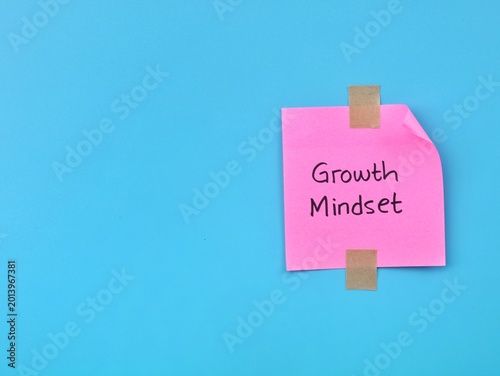 Growth mindset handwritten on pink adhesive note taped on blue background. Symbolizing personal development, motivation, and positive psychological attitude in business or education.