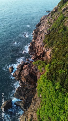 Cinematic aerial footage of ocean surf hitting rocky coast during early morning light. Natural seascape with strong waves and golden sunrise tones