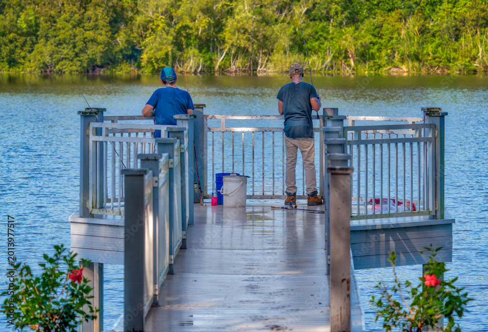 Obraz premium Two men fishing from a dock on a lake