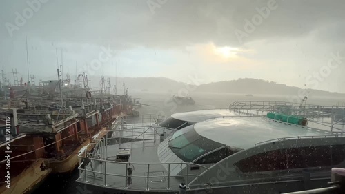 Sunlight n sun ray shine through dramatic stormy rain cloud n dark cloudscape at hobor with Fishing wooden ship n speed boat dock in tropical rainy season climate at raining day on cloudy sky, 4k Aeri