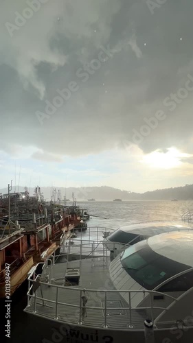 Sunlight n sun ray shine on dramatic stormy rain cloud n dark cloudscape at hobor with Fishing wooden ship n speed boat dock in tropical rainy season climate at raining day cloudy sky, 4k Aerial view 