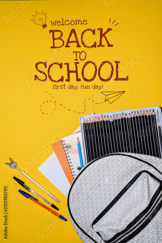School Backpack with Colored Pencils Notebooks and Pens on Yellow Background Top View