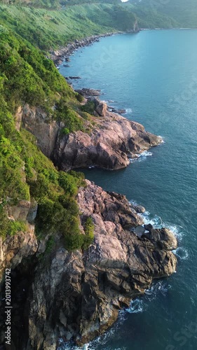 Cinematic aerial footage of ocean surf hitting rocky coast during early morning light. Natural seascape with strong waves and golden sunrise tones