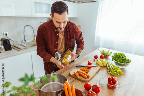 Man Cooking Pasta in Bright Kitchen With Fresh Vegetables and Cutting Board Preparation