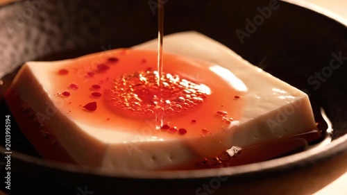Pouring Spicy Chili Oil Onto Silken Tofu in a Dark Bowl, Close Up