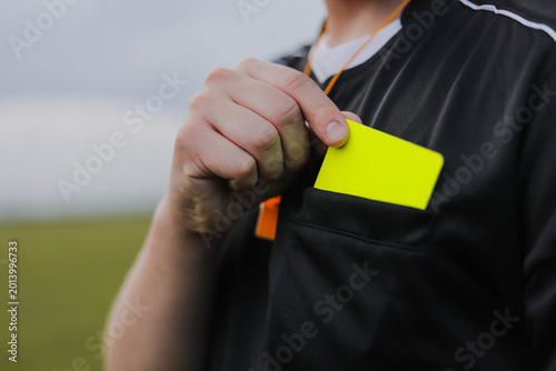 Bild auf Leinwand Soccer referee taking a yellow card from pocket on the field, preparing to penalize a player