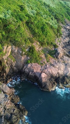 Top view of turquoise sea waves breaking against cliffs at sunrise. Peaceful yet dramatic ocean landscape captured by drone.