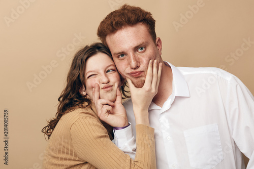 Foto Young couple with playful expressions presses their cheeks together in a warm beige studio