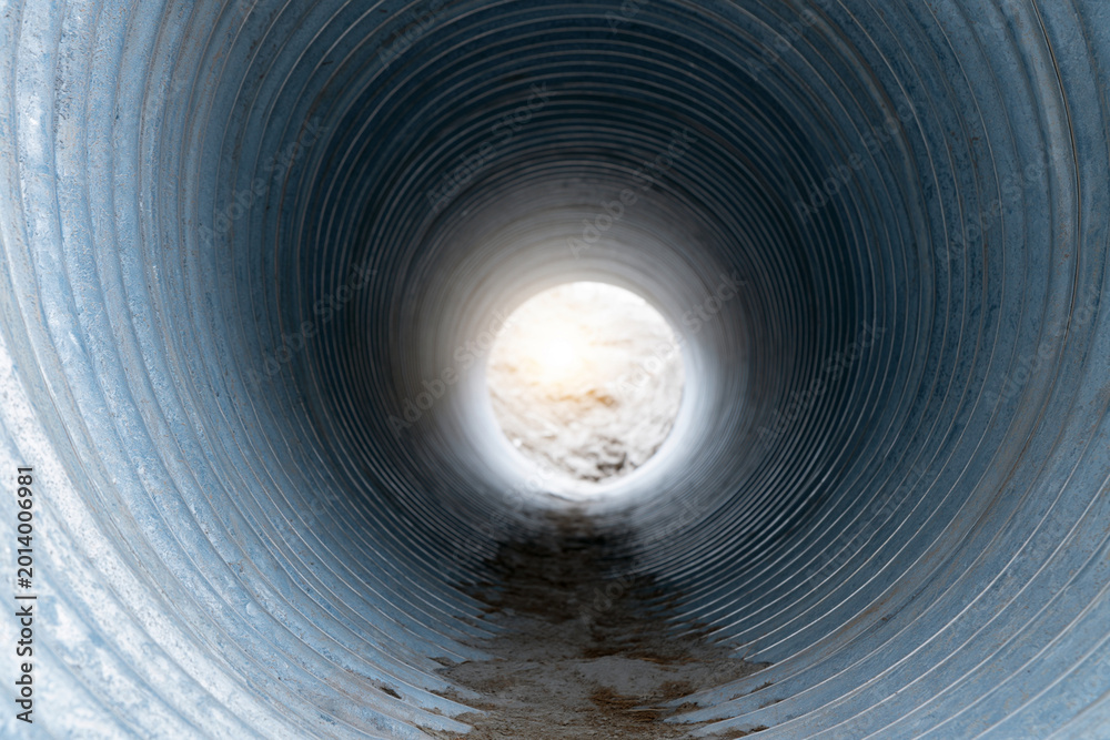 Fototapeta premium Concrete tunnel leads to bright, open sky above. Wet walls show signs of use and time. Dirt stains the floor, hinting at recent passage. View invites curiosity, exploration, or escape