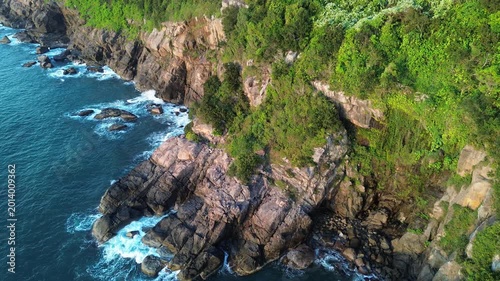 Aerial view of turquoise ocean waves crashing against rocky coastline at sunrise. Cinematic morning seascape with dramatic natural light and powerful waves.