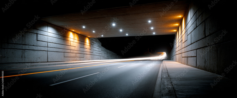 Fototapeta premium Empty urban underpass at night with illuminated concrete walls and light trails from passing vehicles on smooth asphalt road