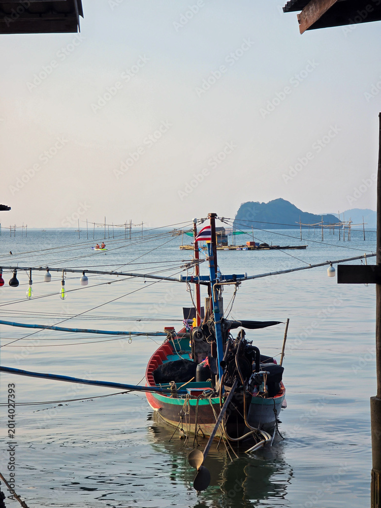 Fototapeta premium Traditional wooden fishing boat resting on calm ocean water creating peaceful scene. Distant island and bright sky complete marine landscape over serene sea reflecting nature perfectly