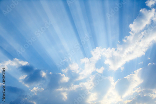 Dramatic blue sky with sun rays shining through white clouds