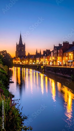 Long exposure shot of a serene river reflecting illuminated buildings under a twilight sky. A church steeple rises over the town