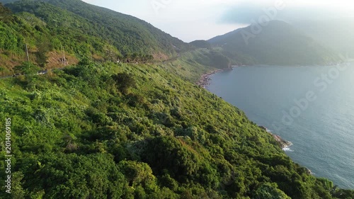 Bird’s eye view of tropical mountains, road, palm trees and sea horizon. Scenic coastal nature landscape with ocean in the distance.