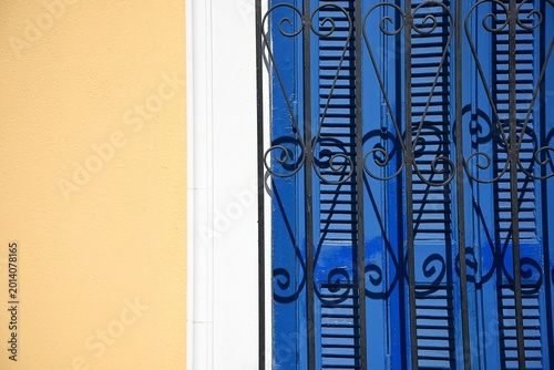 Bild auf Leinwand Old Neoclassical house facade with an ochre stucco wall and a window with blue wooden shutters and handcrafted iron grilles in Anafiotika Athens Greece