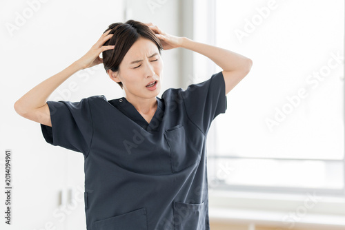頭を抱えて困惑するスクラブを着た日本人女性スタッフ