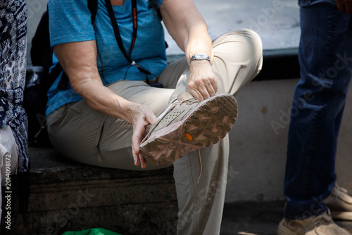 Senior female tourist sitting putting on sneakers, unposed movement, natural candid motion, unposed movement, natural candid motion, close up.