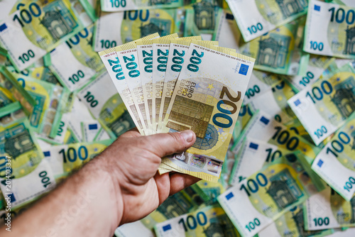 Принти на полотні Macro close-up of hand gripping 200 euro bills with 100 euro banknotes spread in the background
