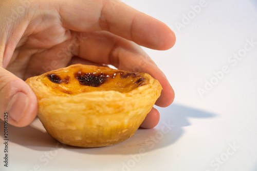 A Hand Holding a Portuguese Egg Tart with Golden Crust and Caramelized Sugar Top