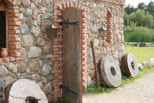 Foto Stone building with wooden door and millstones near grassy area in rural setting