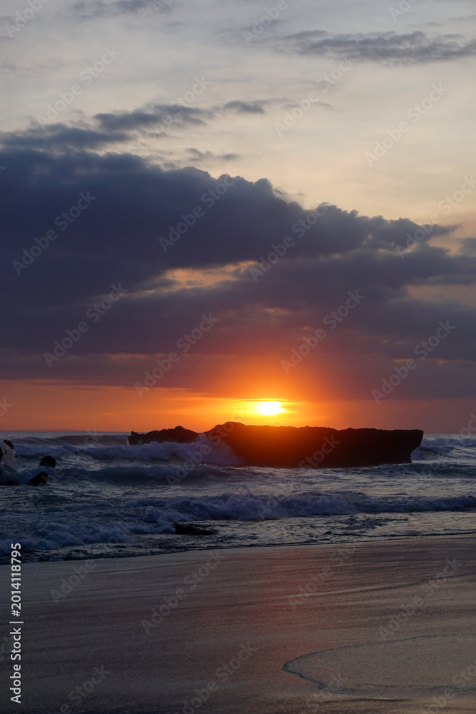 Obraz premium Sunset in the beach. Sun down over sea horizon at sunset with beach view background and dramatic clouds. Sea, sun and sands backgrounds. Vertical. Copy space.