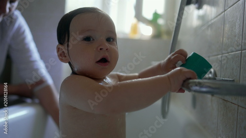 Bild auf Leinwand Baby reaching toward bathtub fixtures while water is poured over head, playful f
