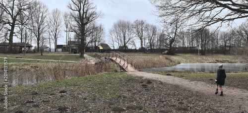 Canvastavla Child walks alone near a small wooden bridge by a pond on a cloudy day in a rura