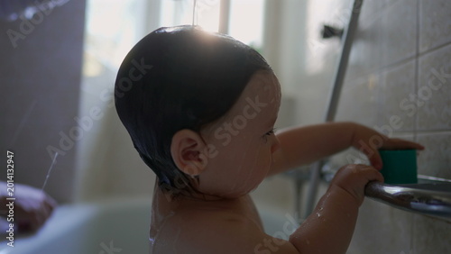 Bild auf Leinwand Baby standing in bathtub holding metal bar with focused playful attention, water