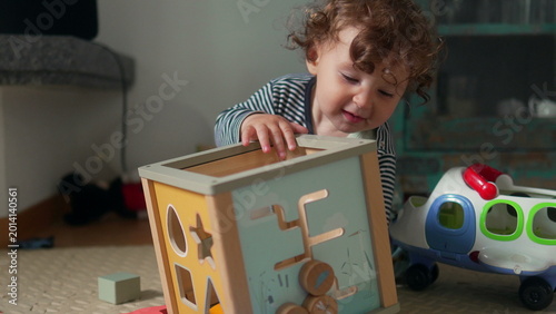 Photos Curly-haired toddler crawling forward toward camera on living room floor, curiou